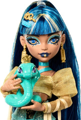 Păpușa Monster High Cleo De Nile într-o bluză aurie și o fustă cu mai multe straturi, include cobra Hissette și accesorii precum un ghiozdan, o gustare și un sul de hârtie igienică, HXH74